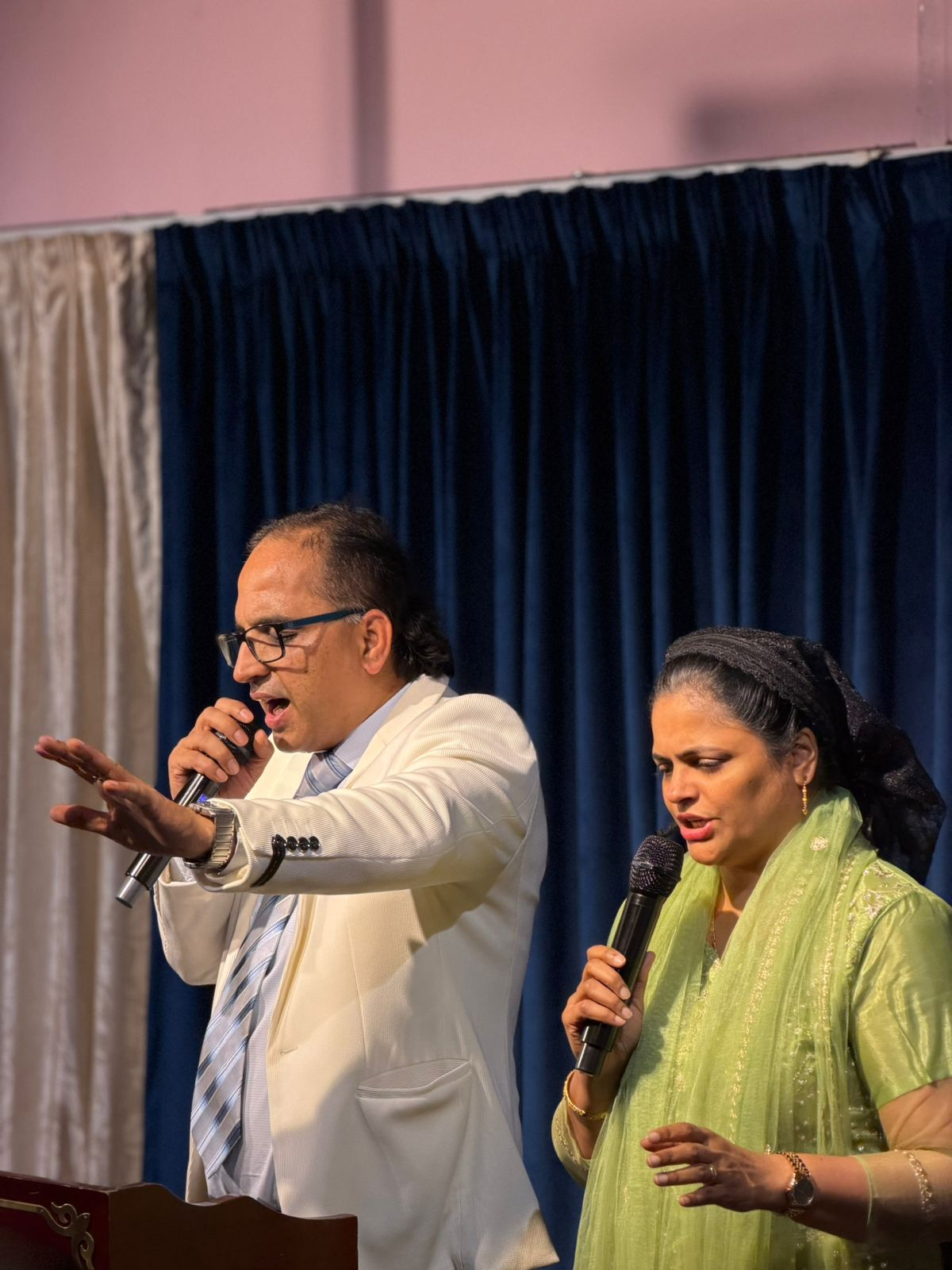 Pastor Roshan and Lavina ministering — hand raised in worship, mic in hand